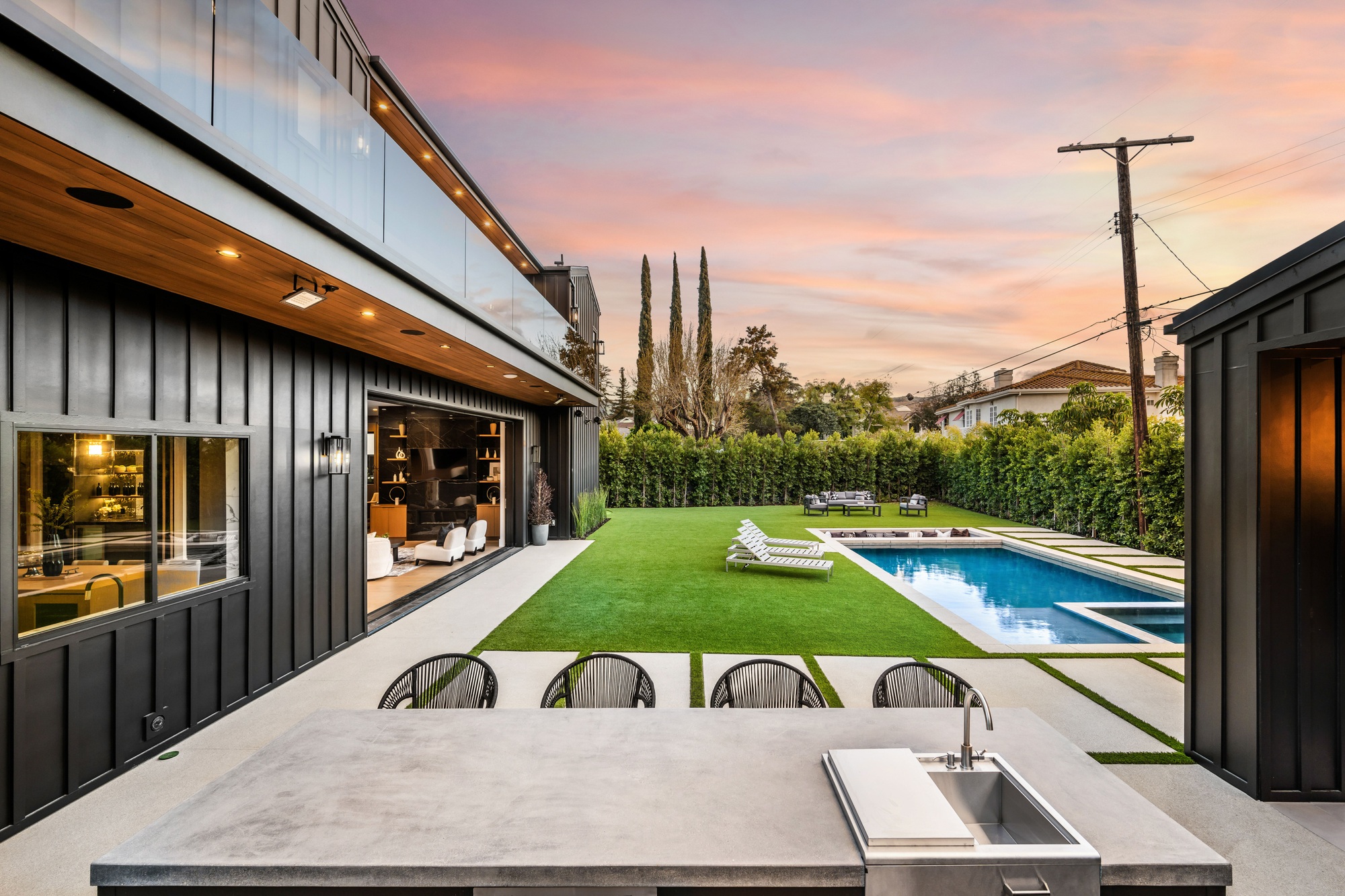 Modern backyard with pool and outdoor kitchen at sunset.